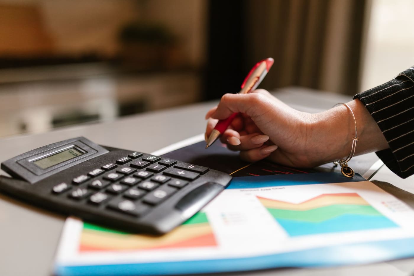 A person using a calculator next to printed charts on a desk