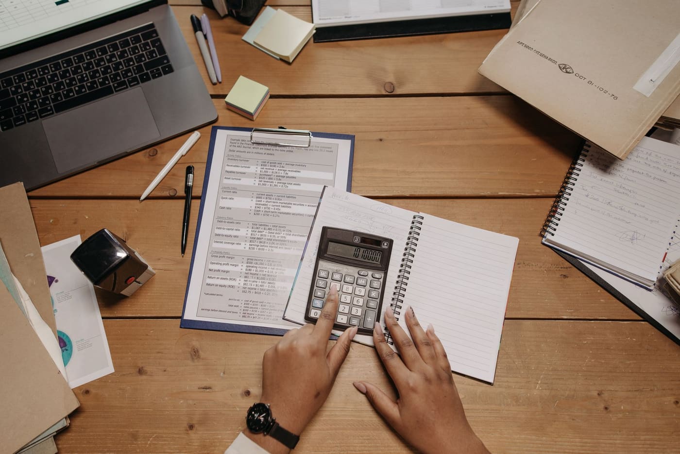 Hands working with a calculator and papers on a wooden desk