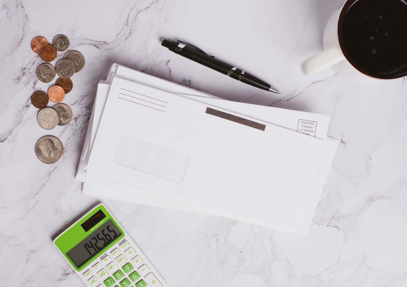 Envelopes, a pen, coins and a calculator on a marble surface