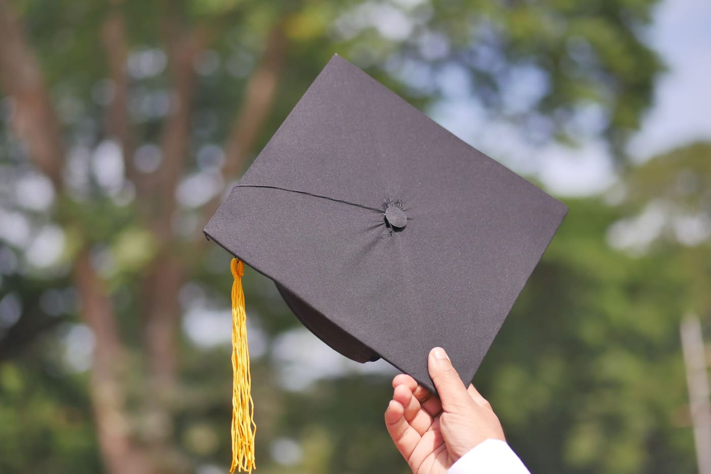 A hand holding up a black graduation cap outdoors
