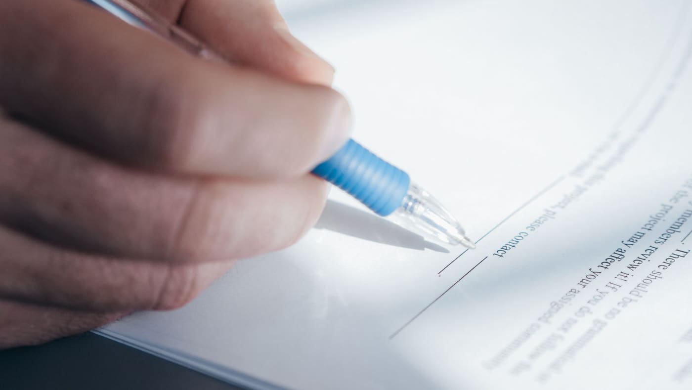 A hand holding a blue pen and signing a document
