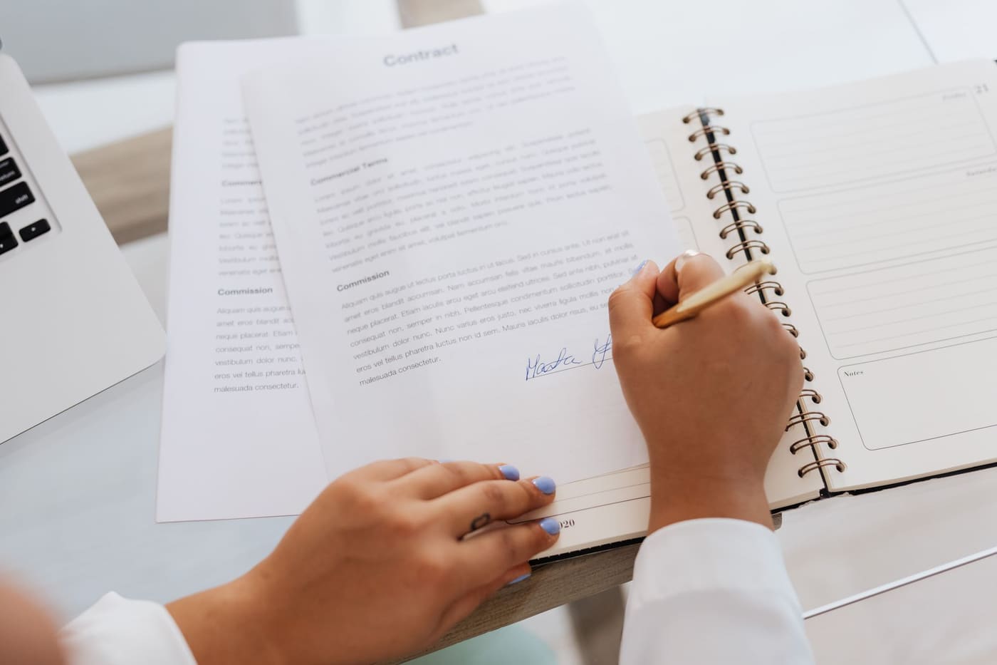 Hands signing papers on a desk next to an open notebook