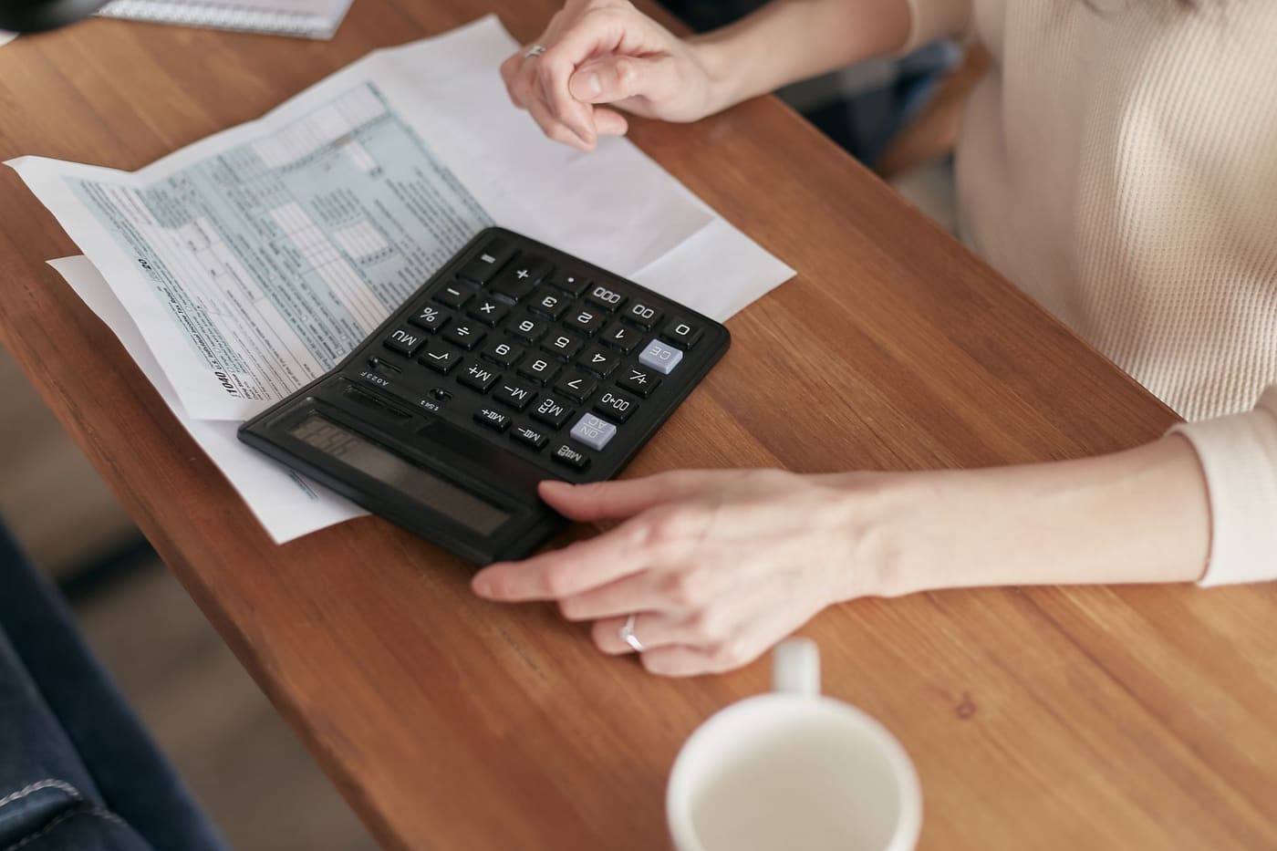 Hands using a calculator with paper statements on a wooden desk