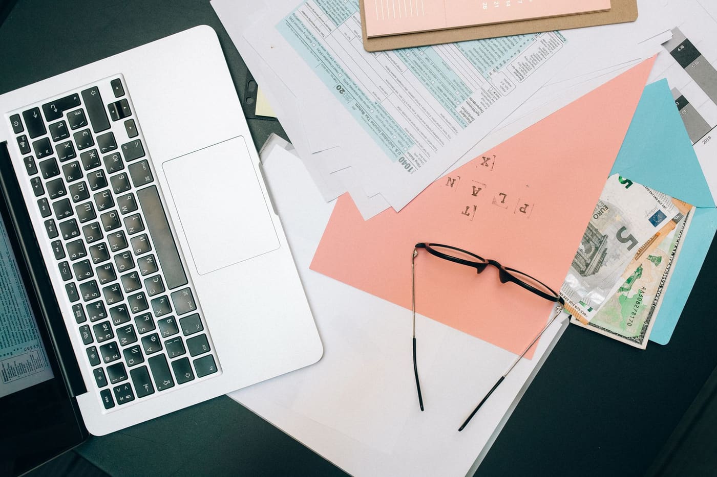 A laptop, paper documents and reading glasses on a desk