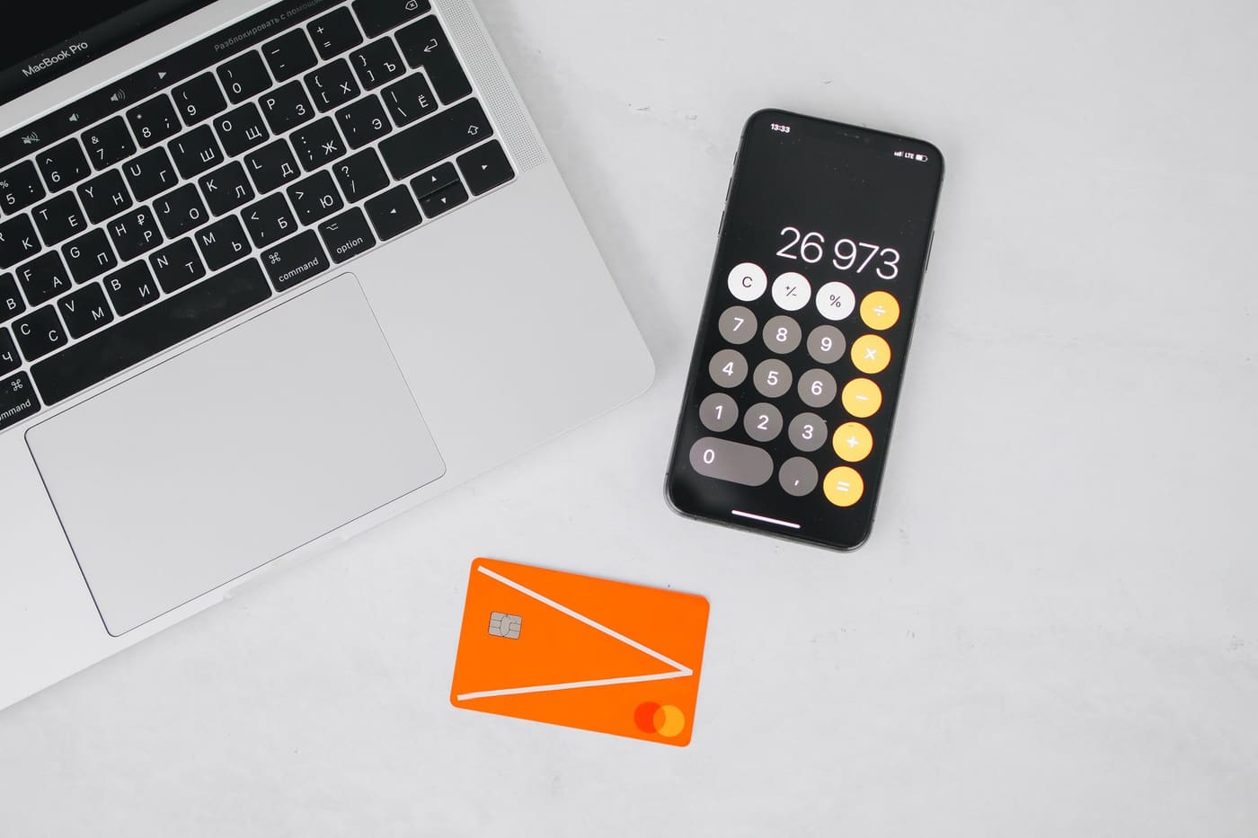 A laptop, a phone showing a calculator and a bank card on a white table