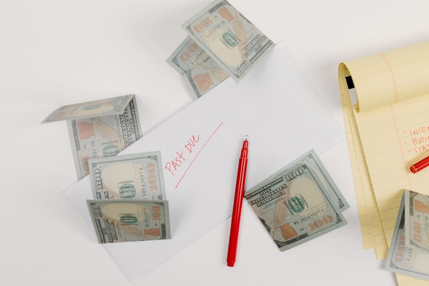 Cash, a red pen and an envelope marked past due seen from above