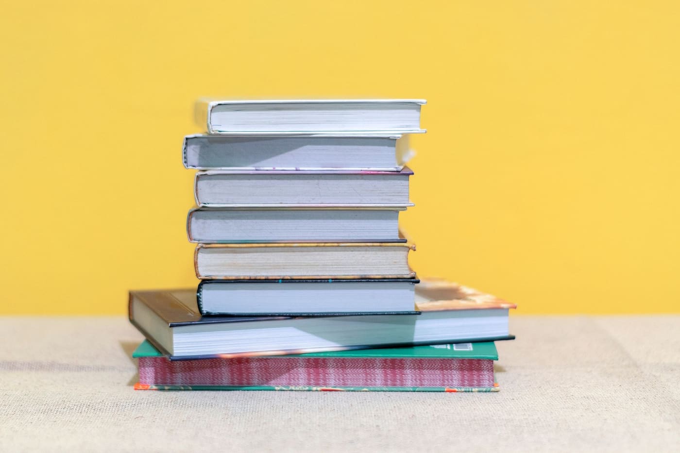 A neat stack of books against a bright yellow wall