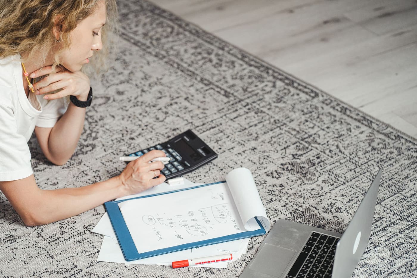 A person working out figures with a calculator and notebook while sitting on a rug